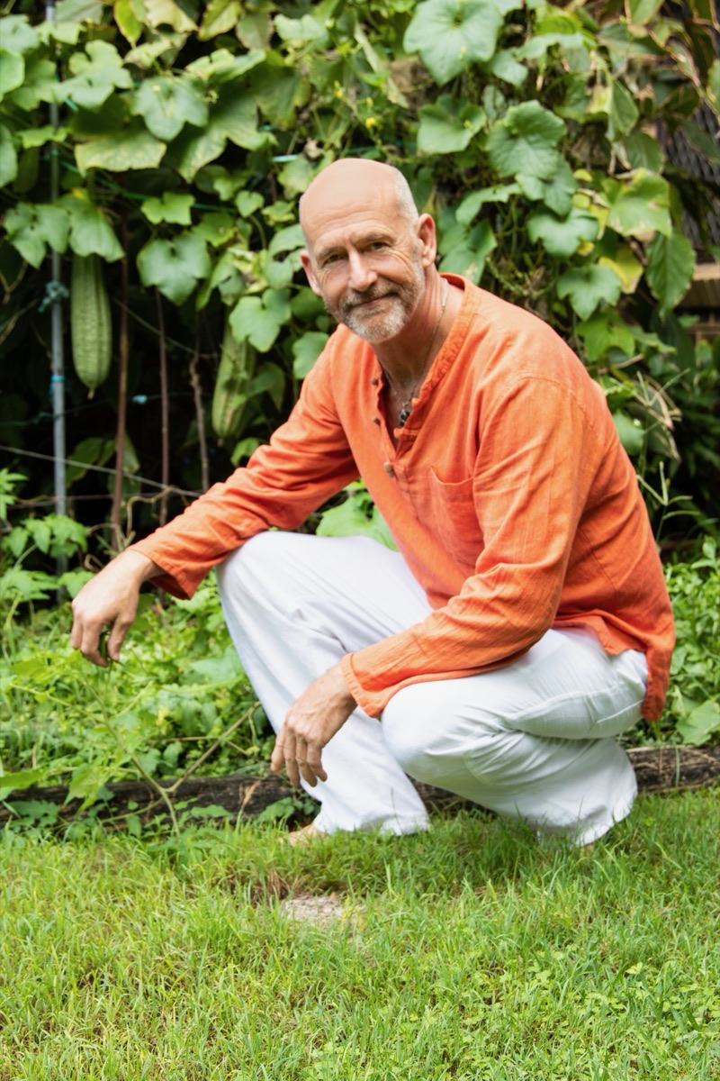 Ed crouching on the grass in a garden, in an orange shirt